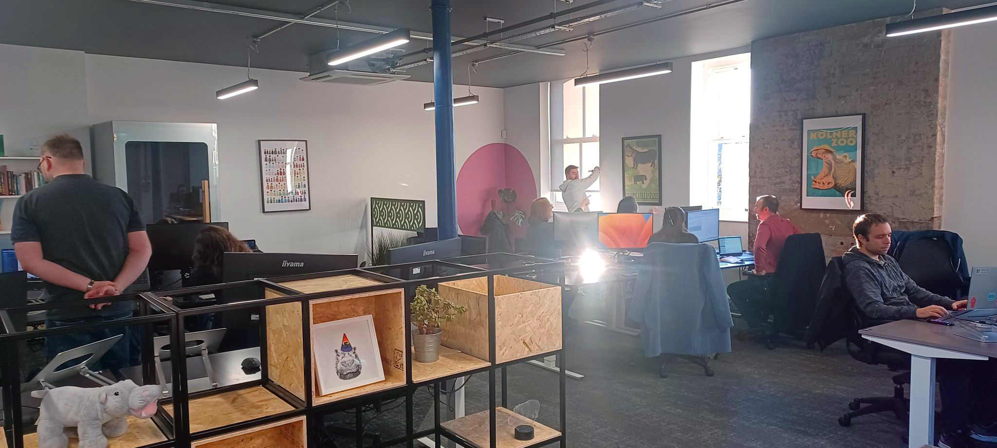 A bright busy office space with several Hippo colleagues in conversation around their work terminals.