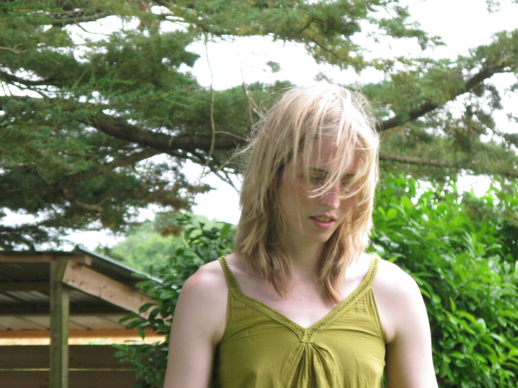 a young woman with blonde hair stood in front of some trees